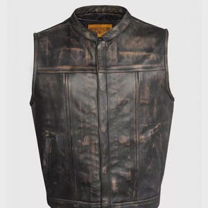 May include: A distressed black leather vest with a stand-up collar and a zip-up front. The vest has a weathered appearance with brown accents and two front pockets. A small tag is visible near the collar.