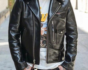May include: A black leather motorcycle jacket with a notched collar, asymmetrical zipper closure, and multiple pockets. The jacket is worn over a white graphic t-shirt. The person is wearing black jeans and has tattoos on their hands.