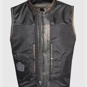 May include: Black vest with a stand-up collar and a front zipper. The vest has a leather-like appearance with a distressed finish and a quilted interior. Features include two front pockets and a small interior pocket.