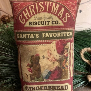 May include: Red and white Christmas themed pillow with the text "Christmas Biscuit Co. Santa's Favorites Gingerbread Cookies". The pillow features a vintage illustration of Santa Claus with a gingerbread man.