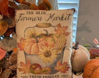 May include: A decorative cushion featuring a vintage illustration of a bucket filled with pumpkins, apples, and corn. The cushion has the text "The Olde Farmers Market" and "Fresh Produce - Pumpkins - Apples - Pie".