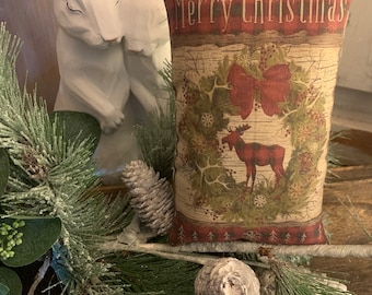 May include: A decorative cushion with a red, green and brown design featuring a moose and a wreath with a red bow. The cushion has the text "Merry Christmas" printed on the front.