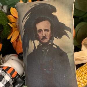 Könnte beinhalten: Ein Dekokissen mit einer Vintage-Illustration von Edgar Allan Poe mit einem Raben auf dem Kopf. Das Kissen hat einen dunkelgrünen Hintergrund und ein Schwarzweißbild von Poe.