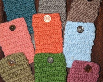 May include: A collection of handmade crochet cozies in various colors, including teal, pink, orange, green, and purple. Each cozy features a button closure. The items are arranged on a dark wooden surface.