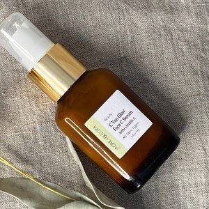 Peut inclure: Une bouteille en verre marron de s&eacute;rum pour le visage avec une pompe blanche et dor&eacute;e. L'&eacute;tiquette indique "C You Glow Face C Serum with Vitamin C" et "ACRE+BLOOM". La bouteille est sur une surface de couleur neutre.