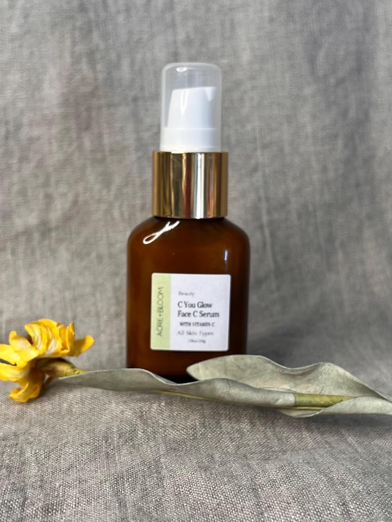 Peut inclure: Une bouteille en verre marron avec une pompe blanche et un col dor&eacute;, &eacute;tiquet&eacute;e "C You Glow Face C Serum with Vitamin C". Une fleur jaune et une feuille verte sont &agrave; c&ocirc;t&eacute; de la bouteille. Le produit est pour tous les types de peau.