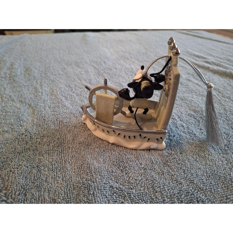 Pode incluir: Estatueta decorativa de um personagem de desenho animado em preto e branco no leme de um barco. O barco &eacute; branco com acabamentos prateados e um volante de madeira. Uma borla prateada pende do topo do barco.