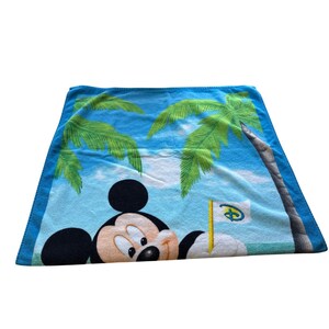 May include: A blue beach towel featuring Mickey Mouse on a tropical beach scene with palm trees and a flag with the Disney logo. The towel has a blue border and is made of a soft, absorbent material.