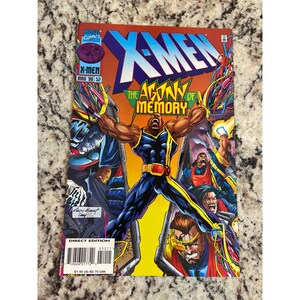 May include: A comic book cover for X-Men, featuring a muscular character in a blue and yellow suit with arms raised. The title "X-Men" is in large, blue letters. The text "The Agony of Memory" is also visible. The comic is a Direct Edition, dated May '96.
