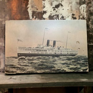 May include: Vintage postcard featuring a black and white illustration of a large passenger ship sailing on wavy water. The ship has multiple decks, smokestacks, and flags. Text at the bottom reads "NIAGARA NAV. CO. NEW STR. CAYUGA."