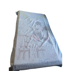 May include: A light blue blanket with a Mickey Mouse design. The blanket has a soft, textured appearance and is folded. The Mickey Mouse graphic is in black, red, and white.