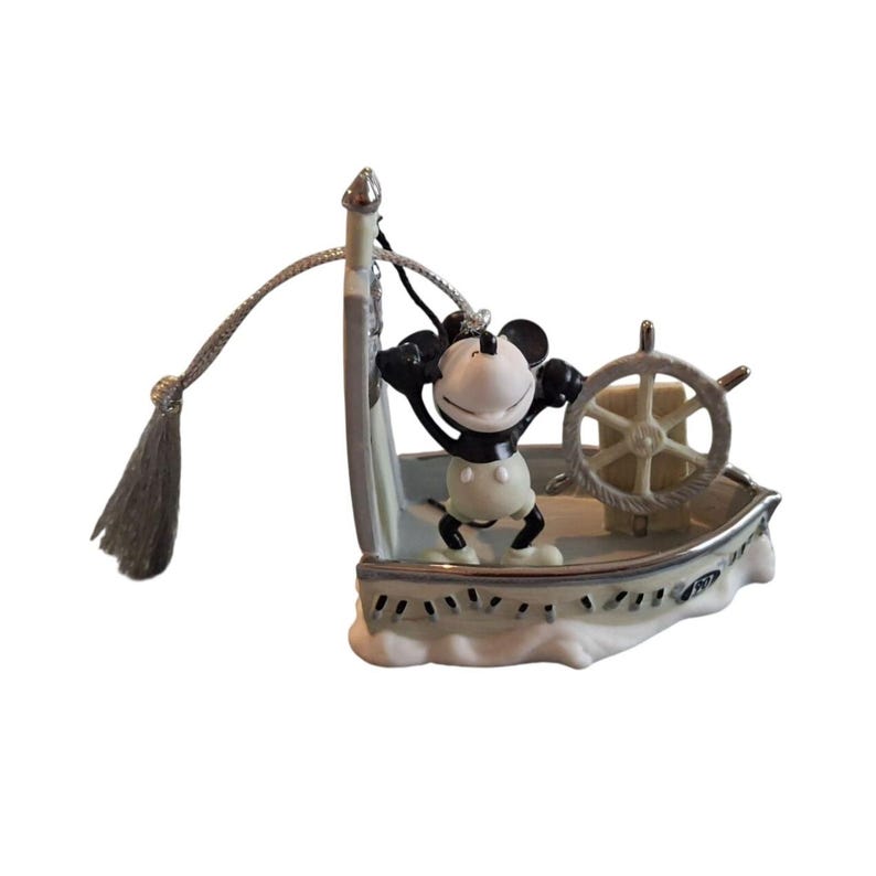 Pode incluir: Estatueta do Mickey Mouse num barco azul claro e branco, com um volante prateado. Mickey usa sua roupa cl&aacute;ssica. O barco &eacute; decorado com detalhes prateados e um cord&atilde;o com borla.