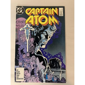 May include: A Captain Atom comic book issue number 2 with a dark blue and purple cover featuring a large central portrait of the character, a smaller figure of Captain Atom above, and various other characters and a city skyline at the bottom.