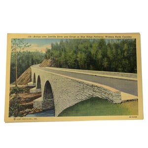 May include: Vintage postcard featuring a stone bridge over a river and gorge on the Blue Ridge Parkway in Western North Carolina. The bridge has multiple arches and a road. The text reads "138-Bridge over Linville River and Gorge on Blue Ridge Parkway, Western North Carolina."