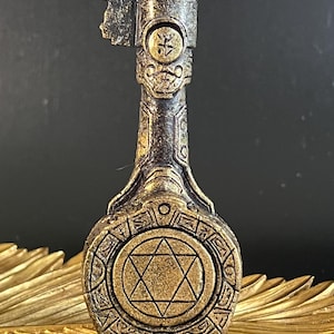 Könnte beinhalten: Dekorative Kerze in Schlüsselform mit Bronze- und Gold-Finish. Das Schlüsseldesign beinhaltet ein Davidstern-Emblem und aufwendige Details. Die Kerze steht auf einem goldfarbenen, blattförmigen Tablett. Höhe ca. 15 cm.