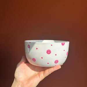 Könnte beinhalten: Weiße Keramikschüssel mit einem pinkfarbenen und weißen Smiley- und Herzmuster.