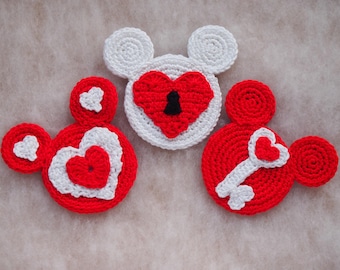 May include: Three crocheted mouse-shaped ornaments with red and white yarn. One ornament has a heart with a keyhole, another has a heart with a key, and the third has a heart with a smaller heart inside.