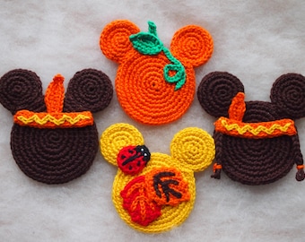 May include: Four crocheted mouse-shaped coasters with different designs. One is orange and has a green leaf, one is yellow with a red ladybug and leaves, and two are brown with orange and yellow trim.