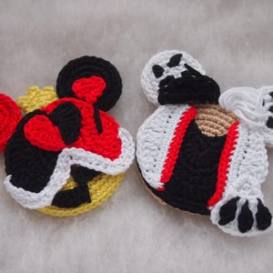 Puede incluir: Dos adornos de personajes de ganchillo, uno con un diseño de corazón rojo y blanco y el otro con un diseño a rayas blanco y negro.