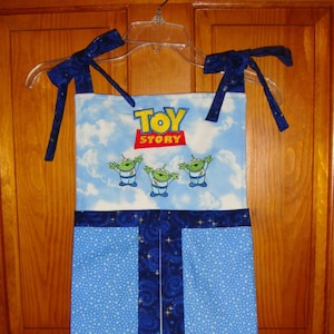 May include: A blue and white diaper caddy with a Toy Story theme. The caddy has a blue and white starry fabric with a blue stripe down the center. The top of the caddy has a white panel with the words "Toy Story" and three green aliens.