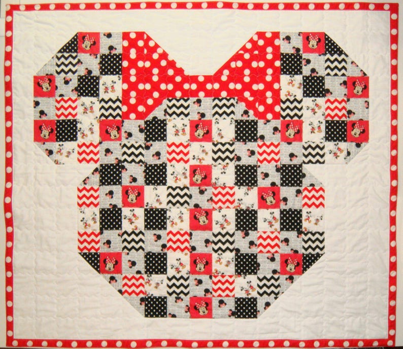 May include: A handmade quilt featuring a Minnie Mouse design. The quilt is shaped like Minnie's silhouette, with a large red polka dot bow. The body is a patchwork of black, white, and red squares with Minnie Mouse images. The border is white with a red polka dot trim.
