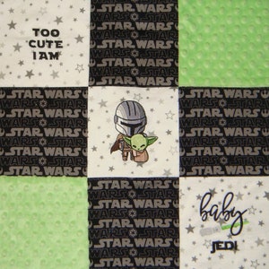 K&ouml;nnte beinhalten: Eine wei&szlig;e, gr&uuml;ne und schwarze Babydecke mit Star Wars-Motiv. Die Decke zeigt ein sich wiederholendes Muster aus "Star Wars" und "Wars Star" in Schwarzwei&szlig;. Das mittlere Quadrat zeigt ein gesticktes Bild eines Mandalorianers und Grogu. Das obere linke Quadrat zeigt den Text "Too Cute I Am" in Schwarzwei&szlig;. Das untere rechte Quadrat zeigt den Text "Baby Jedi" in Gr&uuml;n und Wei&szlig;.