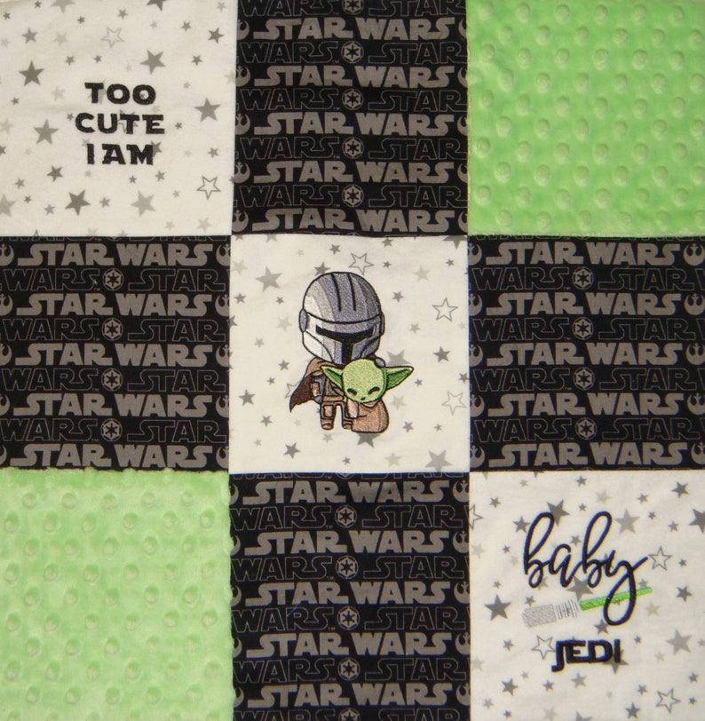 K&ouml;nnte beinhalten: Eine wei&szlig;e, gr&uuml;ne und schwarze Babydecke mit Star Wars-Motiv. Die Decke zeigt ein sich wiederholendes Muster aus "Star Wars" und "Wars Star" in Schwarzwei&szlig;. Das mittlere Quadrat zeigt ein gesticktes Bild eines Mandalorianers und Grogu. Das obere linke Quadrat zeigt den Text "Too Cute I Am" in Schwarzwei&szlig;. Das untere rechte Quadrat zeigt den Text "Baby Jedi" in Gr&uuml;n und Wei&szlig;.