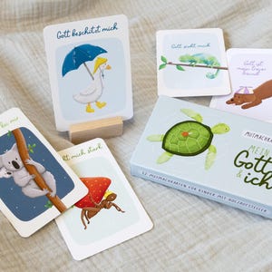 Könnte beinhalten: Ein Set illustrierter Karten und eine Box mit deutschem Text. Die Karten zeigen Tierillustrationen, darunter eine Ente mit Regenschirm, ein Koala, ein Chamäleon, ein Hund, eine Schildkröte und eine Ameise. Die Box hat eine Schildkrötenillustration.