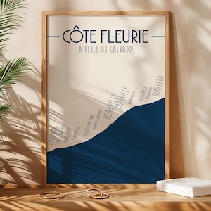 Op de afbeelding: Een ingelijste print met de tekst "CÔTE FLEURIE - LA PERLE DU CALVADOS" in marineblauw. De print heeft een beige achtergrond met een donkerblauw golfontwerp en geeft kustplaatsen weer. De lijst is van licht hout.