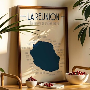 May include: A framed map print of La Réunion, an island in the Indian Ocean, with the text "LA RÉUNION" at the top. The map is dark blue against a cream background, with city names around the island. Two bowls of red berries are in the foreground.