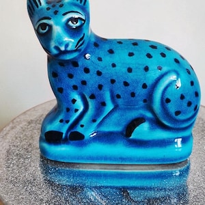 Puede incluir: Figura de cerámica azul de un leopardo con manchas negras. El leopardo está sentado. La figura está sobre una superficie plateada. Objeto decorativo.