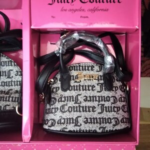 May include: A pink gift box containing a small black and white Juicy Couture handbag. The bag has a repeating logo pattern and gold-colored hardware. The box has the Juicy Couture logo and the text "los angeles, california".