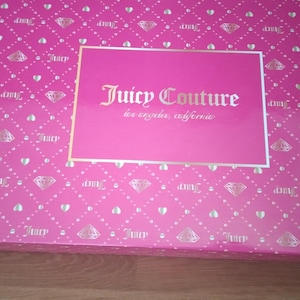May include: A rectangular pink box with a diamond and heart pattern. The box features the text "Juicy Couture los angeles, california" in gold lettering on a pink rectangular label.