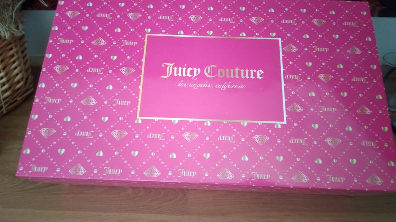 May include: A rectangular pink box with a diamond and heart pattern. The box features the text "Juicy Couture los angeles, california" in gold lettering on a pink rectangular label.