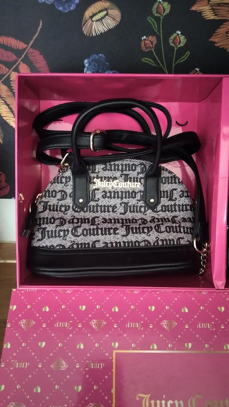May include: A black and white Juicy Couture handbag with a black handle and strap is displayed inside a pink box. The bag features the Juicy Couture logo in a repeating pattern. The box has a diamond and heart pattern.