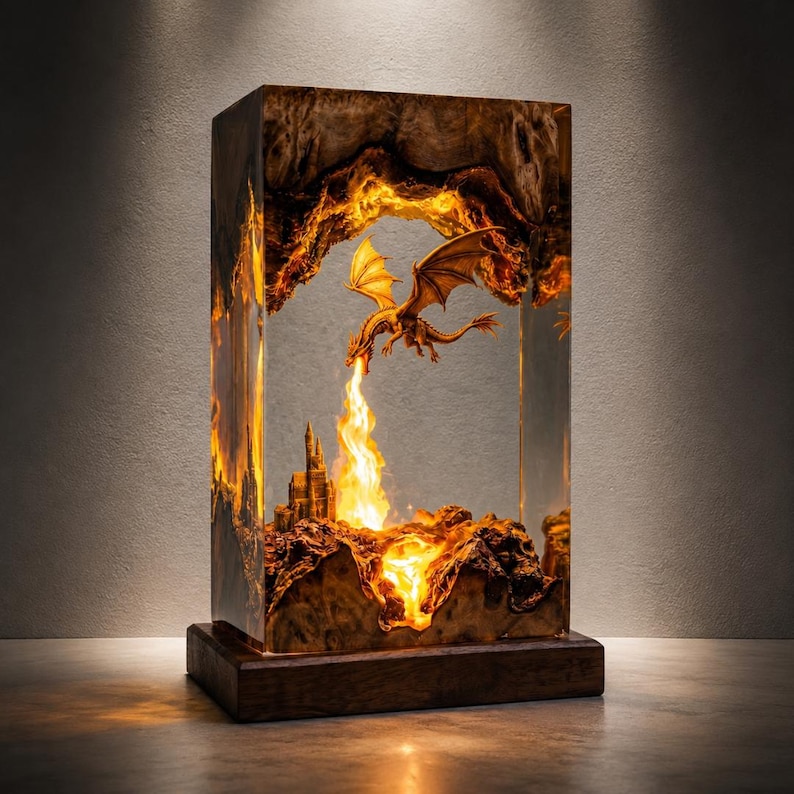 May include: A rectangular lamp made of wood and clear resin featuring an internal scene of a dragon breathing fire toward a castle. The base is dark wood, and the interior is illuminated with a warm orange glow, highlighting the textured wood grain.