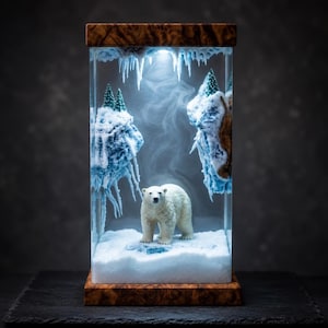 May include: A rectangular resin lamp featuring a white polar bear standing on a snowy base. The scene includes suspended icy rock formations with green pine trees and hanging icicles. The structure is framed by a polished wooden top and base.