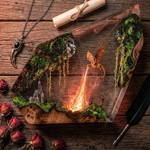 May include: A clear resin display piece featuring a miniature dragon breathing fire over a landscape with green moss, wood, and a small castle. The scene is surrounded by a necklace with a claw pendant, a rolled parchment scroll, and a black quill pen.