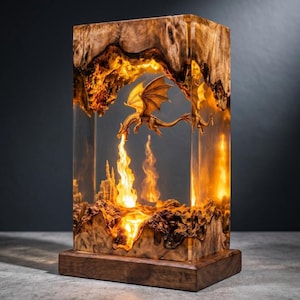 May include: A rectangular lamp made of natural wood burl and clear resin, featuring an illuminated interior scene with a sculpted dragon breathing fire over a miniature castle. The light glows from within, highlighting the wood grain and textures.
