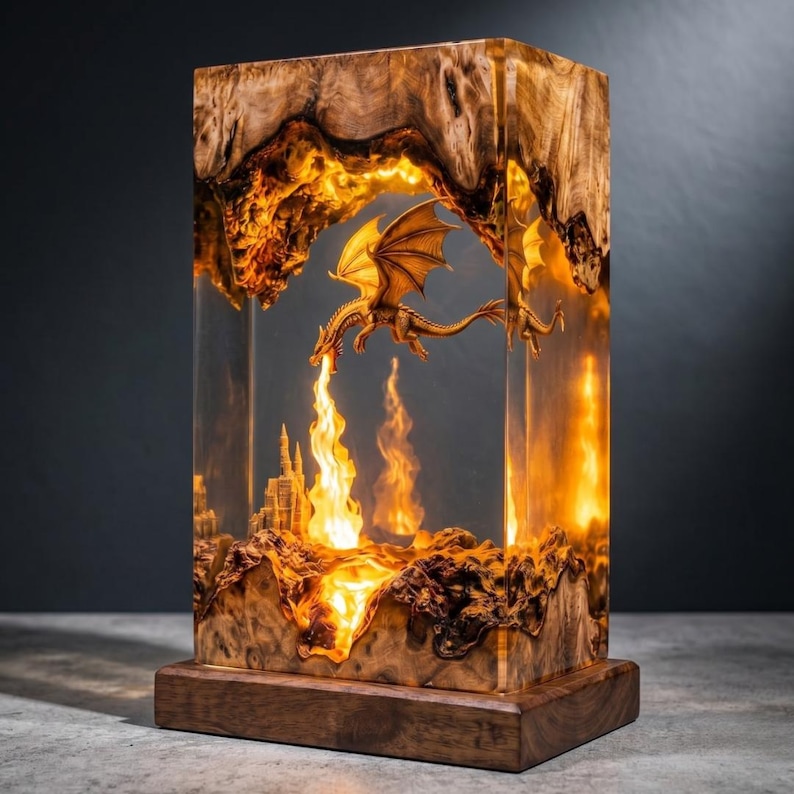 May include: A rectangular lamp made of natural wood burl and clear resin, featuring an illuminated interior scene with a sculpted dragon breathing fire over a miniature castle. The light glows from within, highlighting the wood grain and textures.