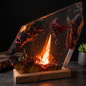 May include: A decorative resin and wood lamp featuring a miniature dragon in flight breathing a bright orange flame toward a rocky landscape. The scene includes a small castle, barren trees, and glowing lava-like veins embedded in the clear resin.