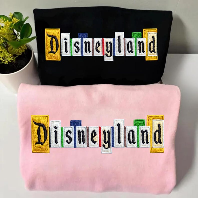 May include: A white ceramic mug with a black handle and the text "But First, Coffee" in a bold, black font. The mug is set against a blurred background. The mug appears to be approximately 10 cm tall.