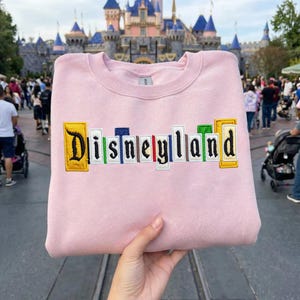 May include: A trio of cream-glazed ceramic mugs with a speckled finish. Each mug is adorned with a hand-painted design: a blue and green leaf, a yellow flower, and a red berry. The mugs have a simple, rounded form.