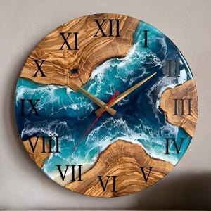 May include: A round wall clock featuring a natural wood grain border and a central resin inlay depicting a turquoise and deep blue ocean scene with white foam waves. The clock face displays black Roman numerals and gold-toned hands.