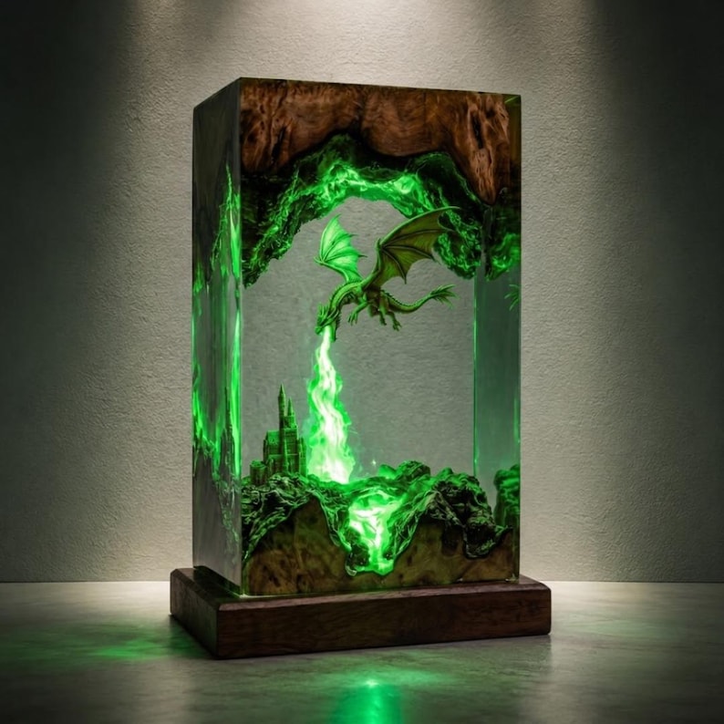 May include: A rectangular lamp featuring a natural wood frame encasing a clear resin block. Inside the resin, a green glowing dragon is suspended above a miniature castle, with a bright green light effect emanating from the dragon toward the castle.