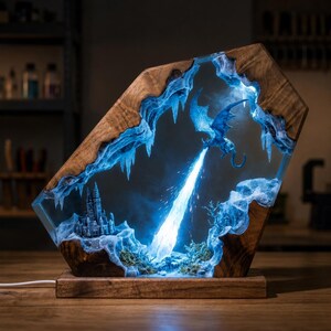 May include: A unique wooden and resin lamp featuring a fantasy scene. The lamp showcases a blue dragon breathing fire towards a castle, with icy blue accents and a wooden frame. The base is a dark wood.