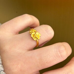 A close-up view of a person's hand wearing a gold ring with a flower design.