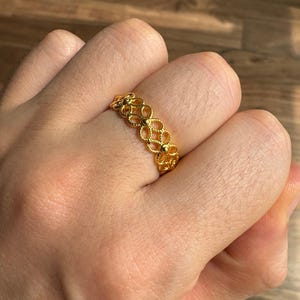 A close-up of a person's hand wearing a gold ring with a floral design.