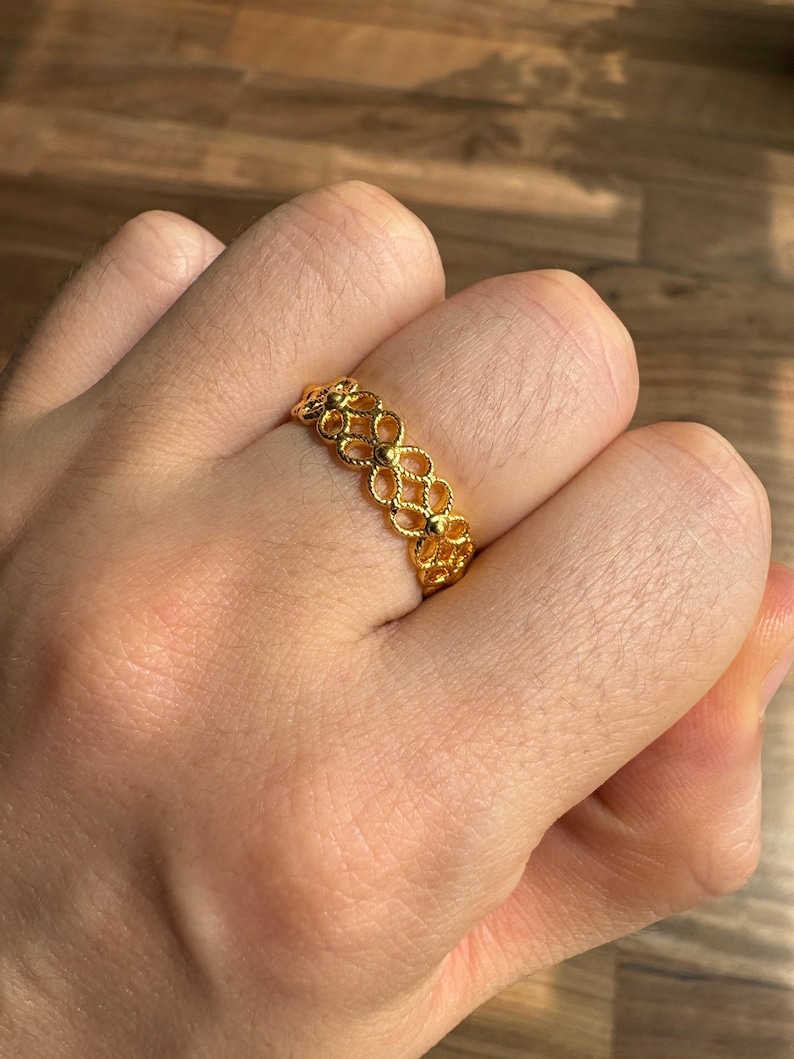 A close-up of a person's hand wearing a gold ring with a floral design.