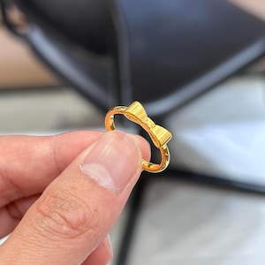 A gold ring with a bow on it is being held in a person's hand.